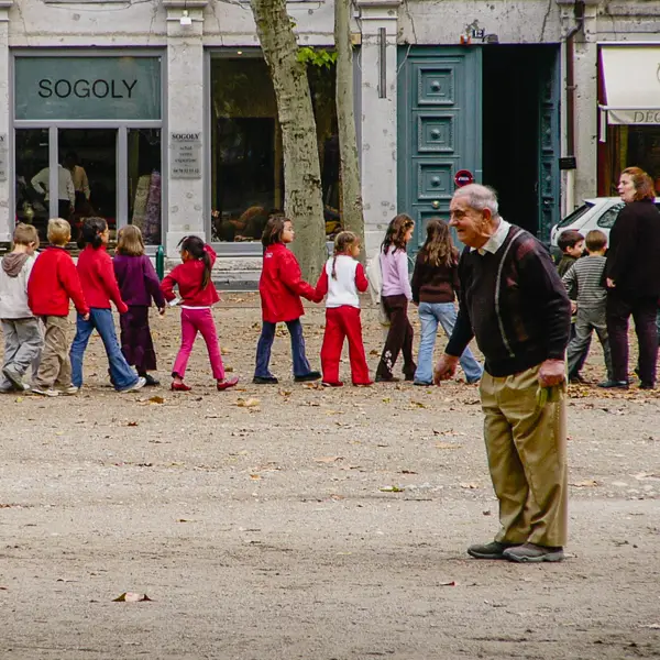 Schoolchildren file past as a man plays péanque in Lyon, France.